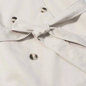 Close-up of a knotted waist belt and tortoiseshell buttons on an off-white trench coat