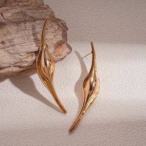 Detailed close-up of golden streamlined stud earrings on weathered wood and textured paper