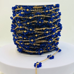 Vista macro di perline di cristallo blu e catena dorata su rotolo per creazione gioielli