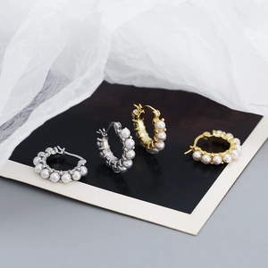 Detailed view of S925 silver and gold pearl hoop earrings on soft white fabric background