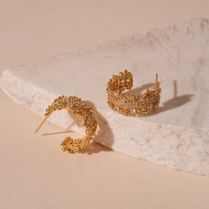 Close-up of gold-plated C-shaped earrings with shimmering cubic zirconia on stone base