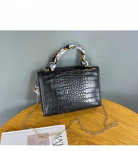 Detail of black crocodile texture bag featuring silk scarf handle and gold chain strap