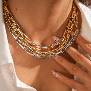 Detail of layered gold and silver mixed chain necklace worn by a model on white shirt
