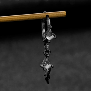Detail of black feather earring with clear gems on wood display, minimalist jewelry style