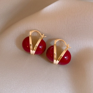 Macro detail of red bead earrings with golden V-shaped frame on satin background