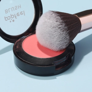 Close-up of peach blush powder with professional brush on soft blue background