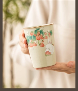 Close-up of hand holding a Ru kiln ceramic tea cup with cute rabbit and strawberry patterns