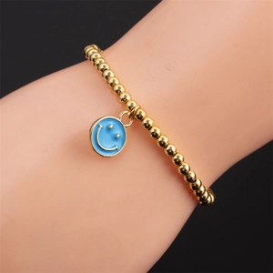 Close-up of gold-plated beaded bracelet with a blue enamel smiley face charm on wrist