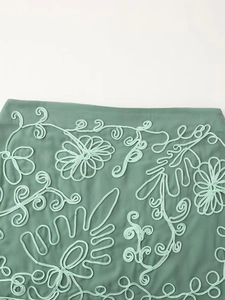 Détail de broderies florales vert menthe et motifs de vigne sur un tissu de style vacances