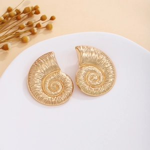 Macro detail of golden spiral conch earrings with vintage brushed texture on a tray