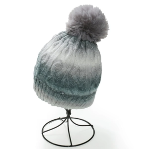 Detail of blue-green gradient knit beanie with thick cable texture and grey faux fur pompom