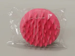 Detail of soft rose red silicone scalp massager brush in its protective transparent packaging