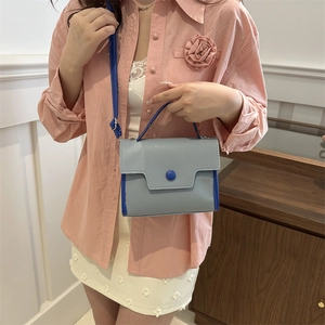 Gray textured crossbody bag with blue contrast trim and round buckle on female model