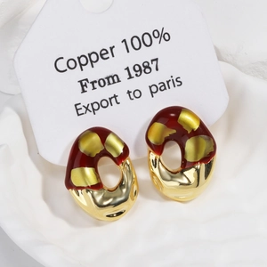 Detailed macro view of an abstract red and gold oval copper earring on a white tray