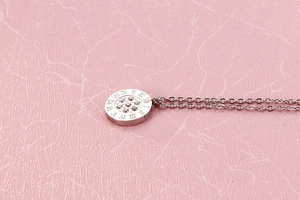 Macro shot of silver circular pendant with crystals and Roman numerals on pink texture