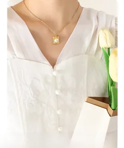 Detailed close-up of a French style gold square pendant necklace with a white pearl inlay