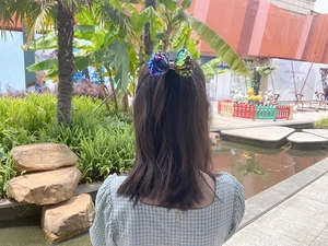 Detail of colorful sequin bow hair clip worn on a half-up hairstyle in outdoor setting