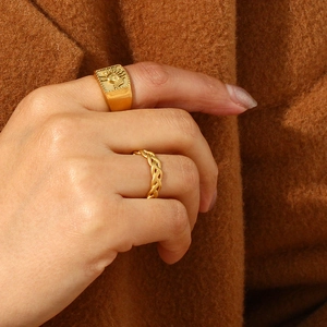 Close-up of gold square sun ring and braided band on a model wearing a brown coat