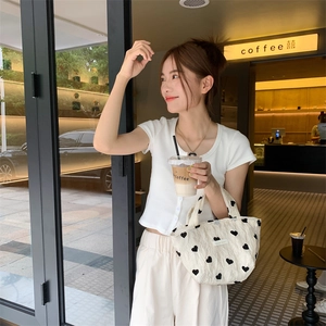 Cream canvas tote bag with black heart patterns and pleated texture held by a model