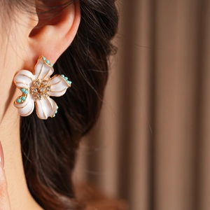 Détail d'une boucle d'oreille vintage à fleurs blanches, perles turquoise et strass dorés