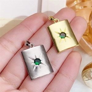 Gold and silver rectangle pendants with green zircon starburst inlay held by hand
