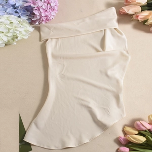 Close-up of beige satin top featuring asymmetric shoulder design and smooth glossy fabric