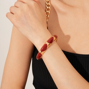 Close-up of a vintage gold-plated cuff featuring red enamel oval accents on a wrist