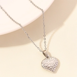 Macro view of a heart-shaped silver pendant with embossed pebble texture on a fine chain
