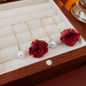 Gros plan de boucles d'oreilles dorées avec roses rouges éternelles et perles blanches