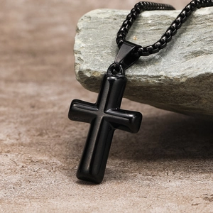 Detail view of a black stainless steel cross pendant on a textured stone surface