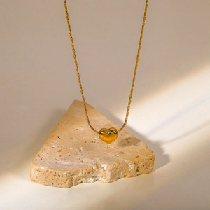 Close-up of a glossy 18K gold-plated heart pendant on a textured stone display
