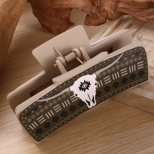 Detail of square beige hair claw clip with a western cow skull pattern on a rustic background