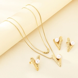Detail view of gold jewelry set featuring V-shaped pendants with white pearls on beige fabric