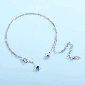 Detailed close-up of a stainless steel heart pendant with a faceted blue gemstone charm