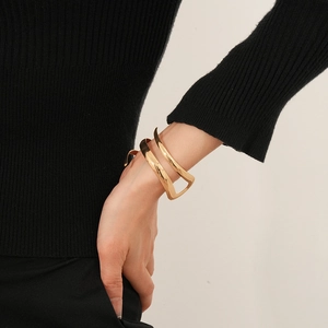 Dettaglio di un bracciale dorato geometrico largo indossato su una manica nera