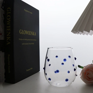 Detailed view of handmade clear glass cup with unique blue raised polka dots on white surface