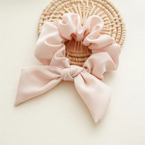 Close-up of pink bow hair tie with silk texture on a rustic woven rattan mat