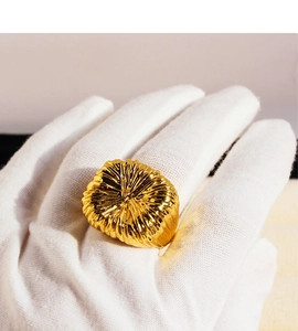 Detail of large gold ring with sunburst pleated texture held by a gloved hand