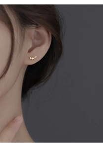 Close-up of curved gold stud earrings with five white zircons on model ear