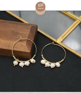 Detail view of gold hoop earrings with white baroque pearls on black background