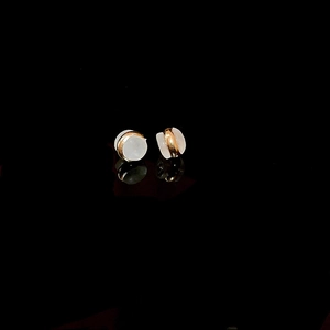 Close-up of gold-rimmed white earrings on reflective surface for detail and texture