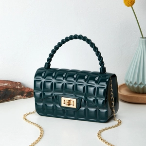 Quilted dark green jelly bag with gold chain strap and turn-lock closure on wooden tray
