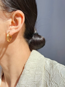 Close-up of a model wearing textured gold-plated hoop earrings with a braided snake chain pattern