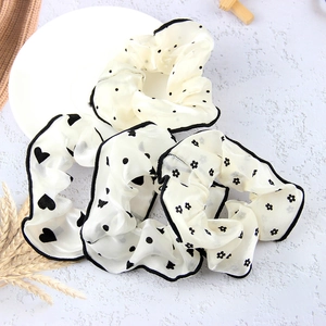 Detail of four white organza hair scrunchies with black polka dots and heart patterns