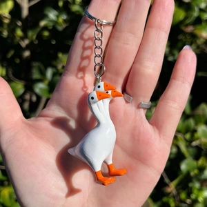 Quirky creative three-headed white goose keychain with orange beak in sunlight