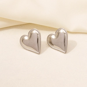 Macro detail of 3D heart-shaped stainless steel earrings on a soft beige silk fabric
