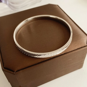 Macro shot of silver textured bangle with honeycomb pattern on a brown silk gift box