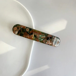 Detail of green and brown tortoiseshell acetate hair clip with floral rhinestones
