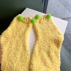 Detail of warm yellow coral fleece socks with 3D cartoon eyes and green pom poms