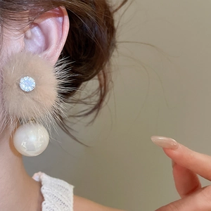 Detail of earring with a fluffy light brown pompom, sparkling crystal, and a white pearl
